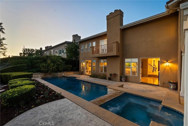 pool at dusk with a patio and an in ground hot tub