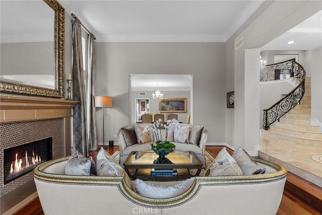 living room featuring wood-type flooring, crown molding, a fireplace, and a chandelier