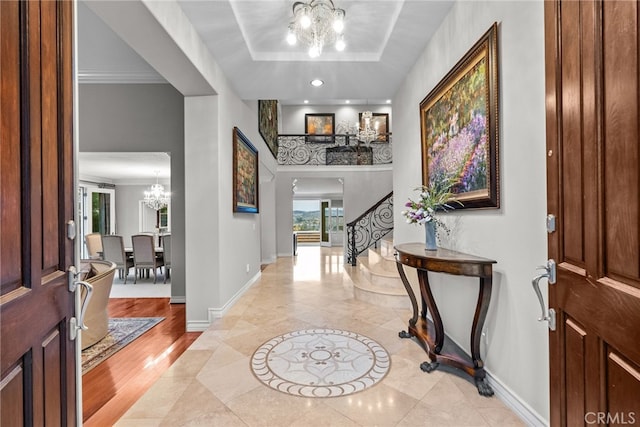 foyer entrance featuring a notable chandelier, crown molding, a raised ceiling, and light wood-type flooring