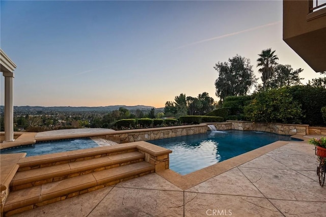 pool at dusk with an in ground hot tub, pool water feature, and a patio area