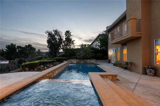 pool at dusk with pool water feature and a patio area