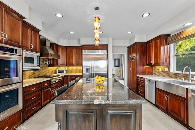 kitchen with pendant lighting, wall chimney exhaust hood, built in appliances, and a kitchen island