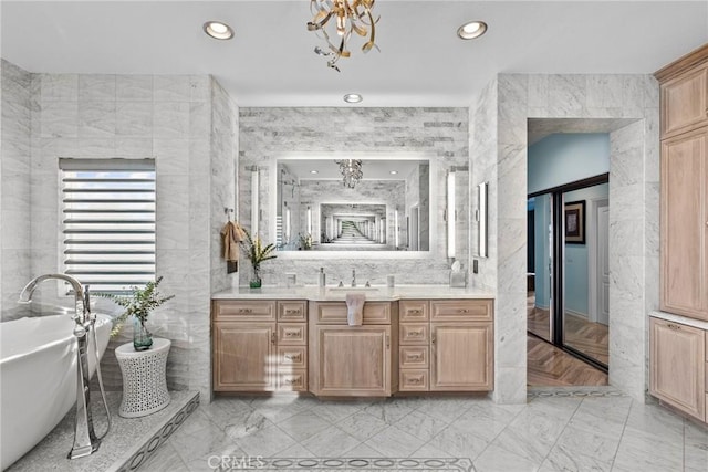 bathroom with an inviting chandelier, vanity, tile walls, and a tub