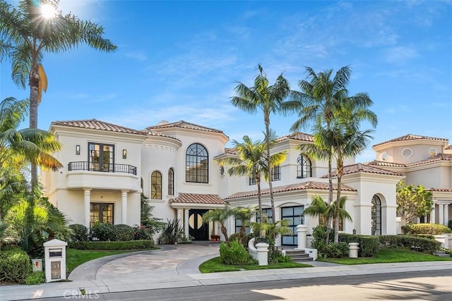 mediterranean / spanish home with driveway, a balcony, a tiled roof, and stucco siding