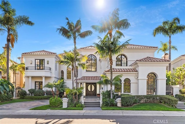 mediterranean / spanish home with concrete driveway, a tile roof, a balcony, and stucco siding