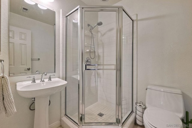 bathroom with a shower with door, sink, and toilet