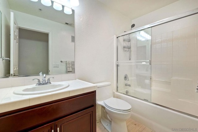 full bathroom featuring vanity, shower / bath combination with glass door, and toilet