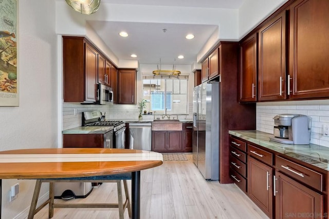 kitchen with appliances with stainless steel finishes, sink, light wood-type flooring, and decorative backsplash