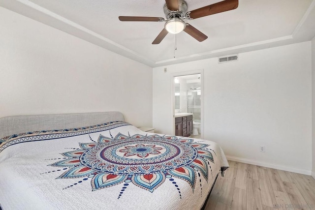 bedroom with a tray ceiling, light hardwood / wood-style flooring, ceiling fan, and ensuite bathroom