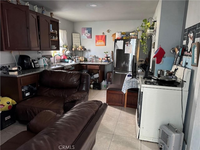 kitchen with sink, dark brown cabinets, light tile patterned floors, stainless steel fridge, and white gas range oven