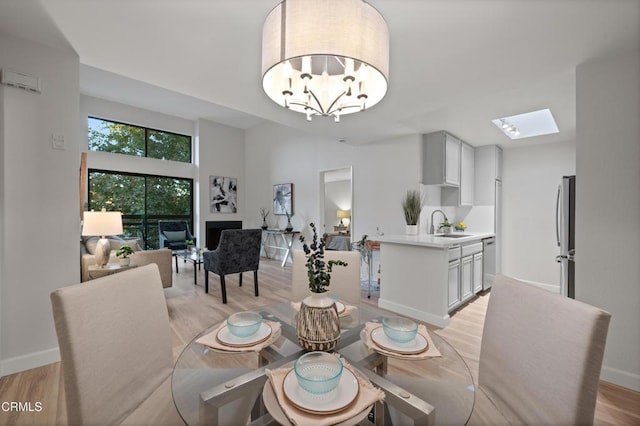 dining room featuring light hardwood / wood-style flooring, sink, a skylight, and an inviting chandelier