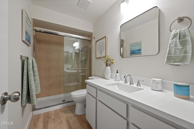 bathroom with vanity, toilet, a shower with shower door, and hardwood / wood-style floors