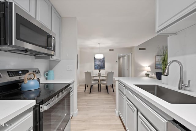 kitchen featuring appliances with stainless steel finishes, sink, light hardwood / wood-style floors, and decorative light fixtures