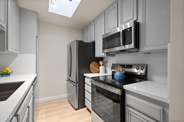 kitchen featuring sink, a skylight, gray cabinets, stainless steel appliances, and light hardwood / wood-style floors