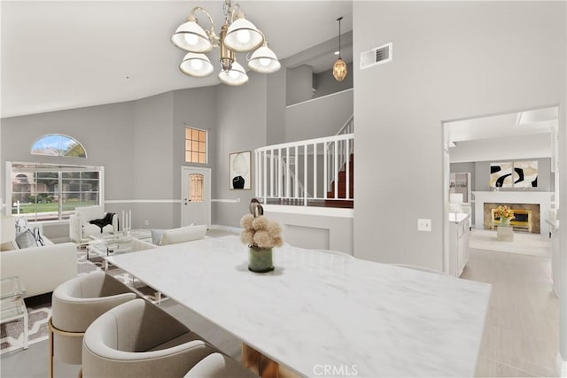 dining area featuring stairway, visible vents, high vaulted ceiling, a fireplace, and a notable chandelier