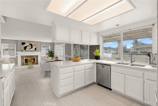 kitchen featuring a fireplace, a peninsula, stainless steel dishwasher, white cabinets, and a sink