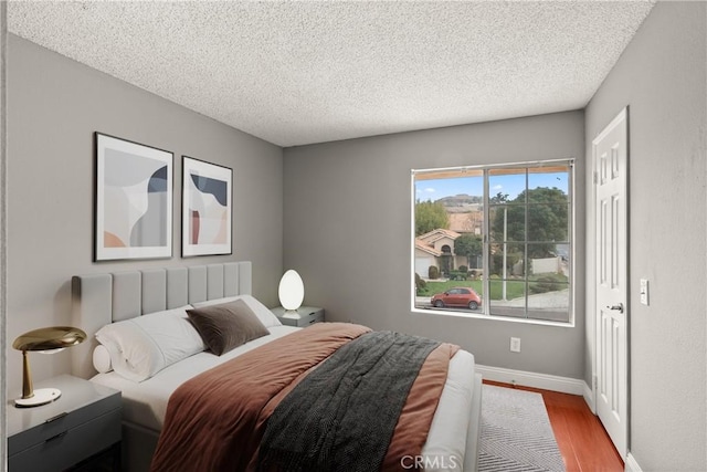 bedroom with wood finished floors, baseboards, and a textured ceiling