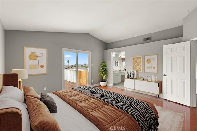 bedroom featuring visible vents, wood finished floors, ensuite bath, access to exterior, and vaulted ceiling