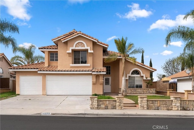 mediterranean / spanish house featuring a tiled roof, stucco siding, driveway, and fence