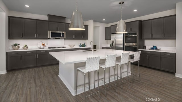 kitchen with appliances with stainless steel finishes, decorative light fixtures, sink, a kitchen bar, and a center island with sink