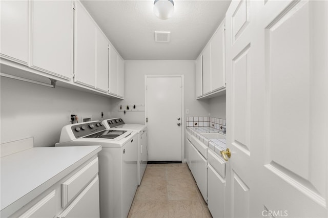 clothes washing area with cabinets, a textured ceiling, and washer and clothes dryer