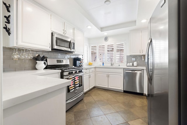 kitchen featuring sink, a raised ceiling, white cabinets, stainless steel appliances, and backsplash