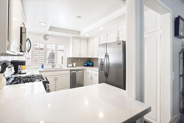 kitchen with a raised ceiling, appliances with stainless steel finishes, white cabinets, and kitchen peninsula