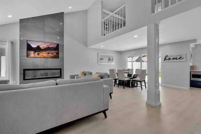 living room with a towering ceiling, a fireplace, and light hardwood / wood-style floors