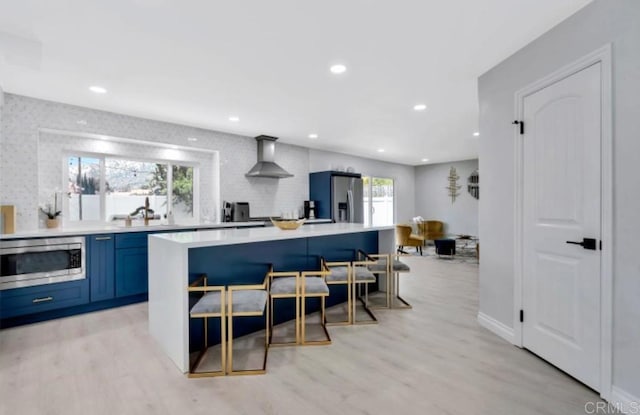 kitchen featuring blue cabinets, sink, appliances with stainless steel finishes, light hardwood / wood-style floors, and wall chimney range hood