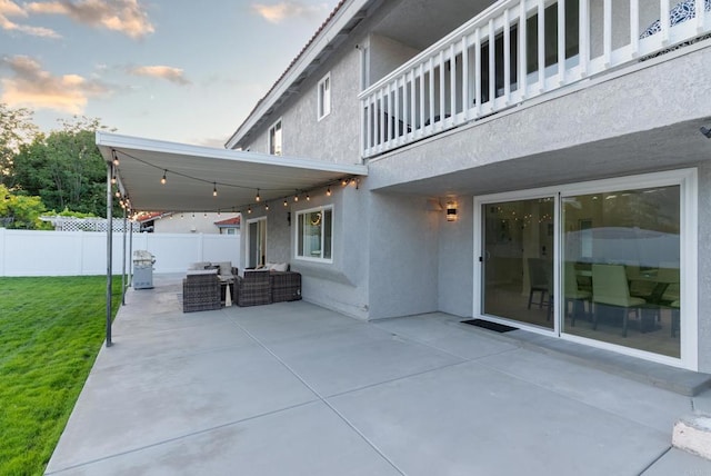 patio terrace at dusk featuring an outdoor hangout area, a balcony, and a lawn