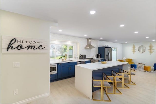 kitchen with sink, a kitchen bar, light hardwood / wood-style floors, stainless steel appliances, and wall chimney exhaust hood