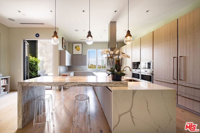 kitchen featuring pendant lighting, light brown cabinetry, a breakfast bar area, and oven