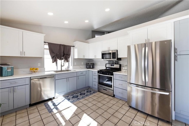 kitchen with appliances with stainless steel finishes, sink, light tile patterned floors, gray cabinets, and white cabinets