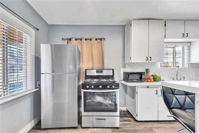 kitchen featuring wood-type flooring, sink, white cabinets, backsplash, and stainless steel appliances