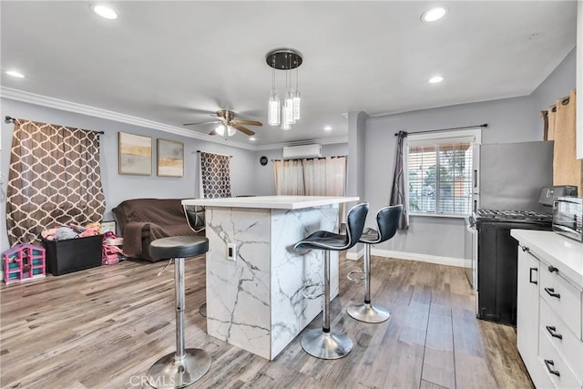 kitchen with an AC wall unit, black gas range oven, a breakfast bar area, white cabinets, and hanging light fixtures