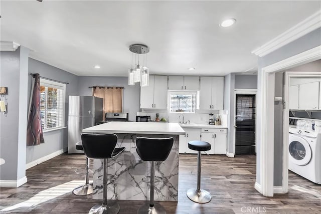 kitchen featuring dark hardwood / wood-style floors, pendant lighting, stainless steel refrigerator, washer / dryer, and white cabinets