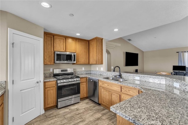 kitchen with sink, light stone counters, light hardwood / wood-style flooring, appliances with stainless steel finishes, and kitchen peninsula