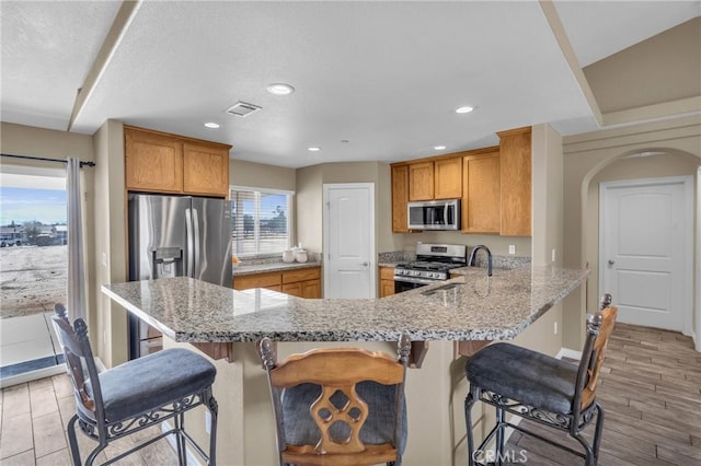 kitchen with appliances with stainless steel finishes, light stone counters, a kitchen bar, and kitchen peninsula