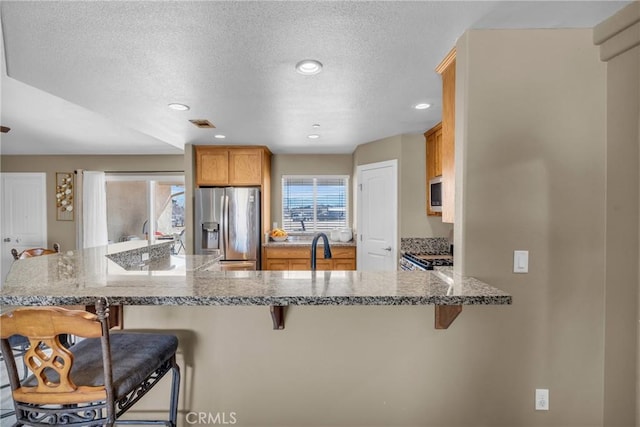 kitchen with appliances with stainless steel finishes, a breakfast bar, light stone counters, and kitchen peninsula