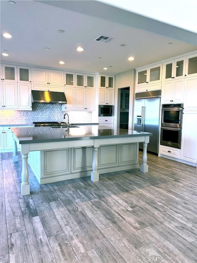 kitchen featuring built in appliances, hardwood / wood-style flooring, an island with sink, and a breakfast bar