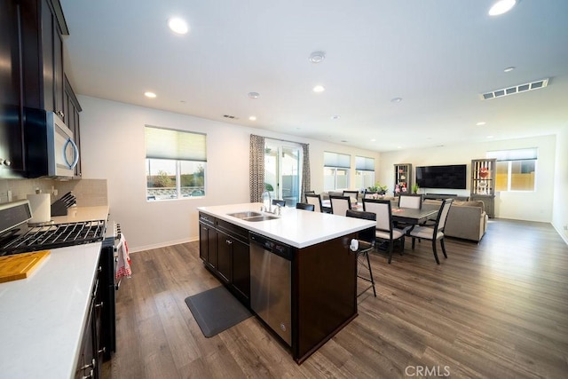 kitchen featuring sink, dark wood-type flooring, appliances with stainless steel finishes, a center island with sink, and decorative backsplash