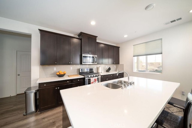 kitchen with sink, a breakfast bar area, stainless steel appliances, dark brown cabinetry, and a center island with sink