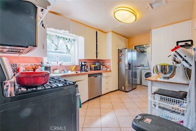 kitchen featuring white cabinetry, light tile patterned floors, washer and dryer, and appliances with stainless steel finishes