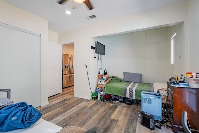 bedroom with hardwood / wood-style flooring, ceiling fan, and stainless steel refrigerator with ice dispenser