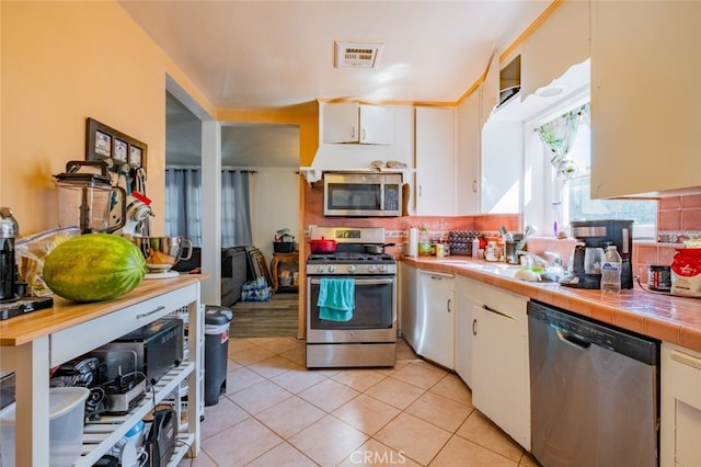 kitchen with white cabinetry, appliances with stainless steel finishes, tile counters, and backsplash