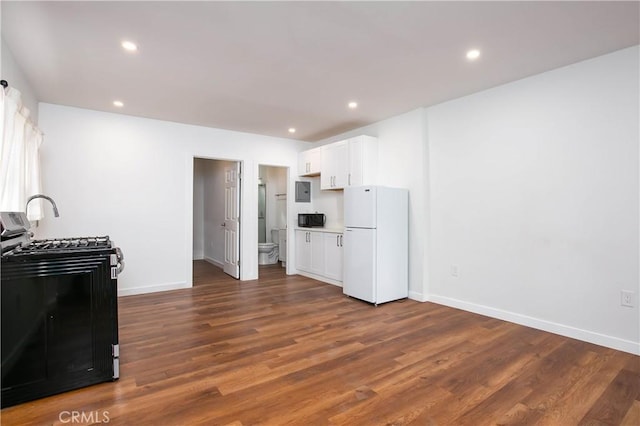 kitchen featuring dark hardwood / wood-style flooring, gas range oven, white fridge, and white cabinets