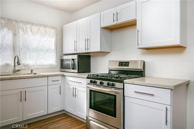 kitchen with stainless steel appliances, sink, white cabinets, and light hardwood / wood-style floors