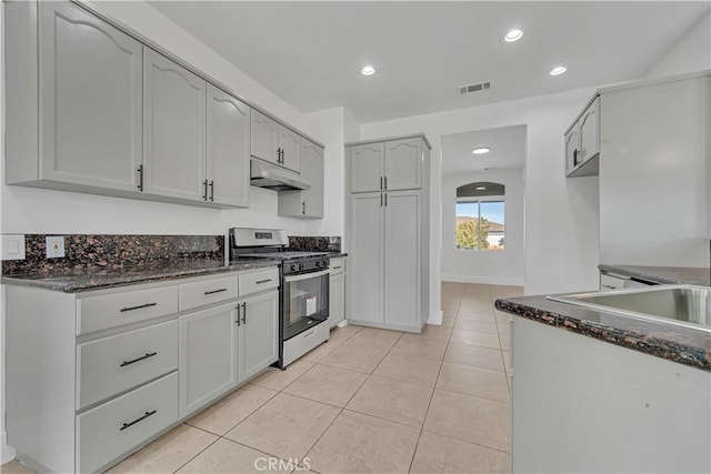 kitchen featuring gas range, dark stone countertops, and light tile patterned floors