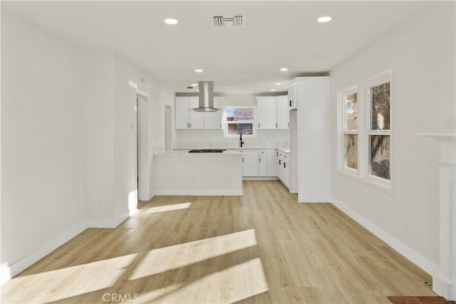 kitchen featuring stovetop, sink, white cabinets, island exhaust hood, and light wood-type flooring