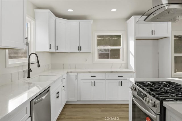 kitchen with extractor fan, white cabinetry, sink, light stone counters, and stainless steel appliances